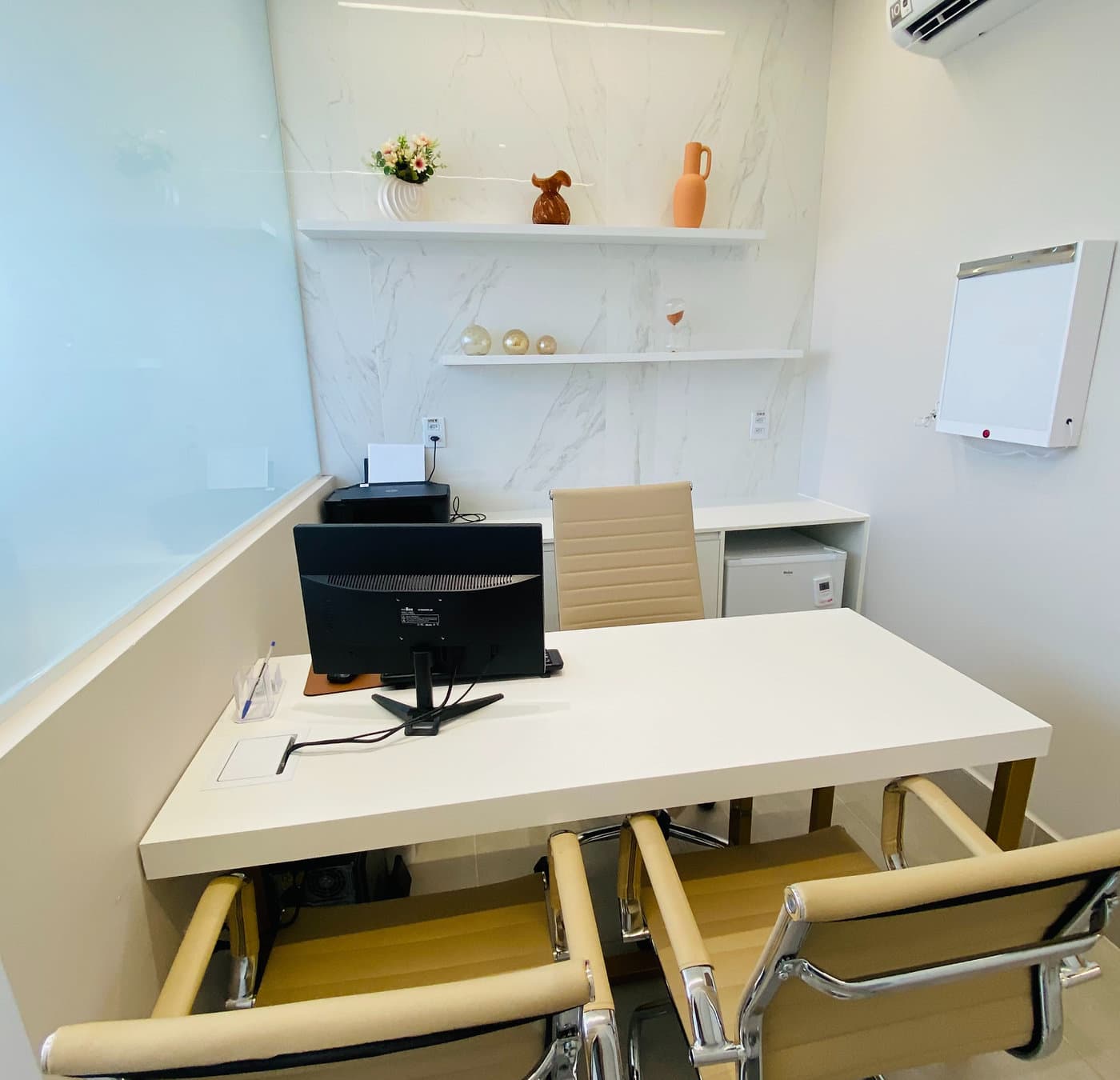 Consultório da unidade Prado do Instituto Hiraki: mesa branca, cadeiras, prateleiras e negatoscópio na parede